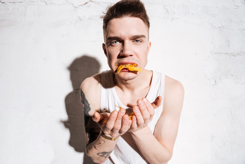 Man with opened mouth full of potato chips over white background for how to keep healthy article