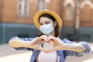 Happy girl in Covid mask making a heart shape with her hands