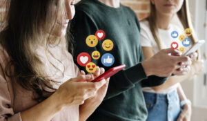 Three people on phones with emojis coming out of screen to signify likes etc. For online safety article