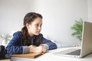 Teenage girl sat in front of computer taking notes for remote learning tips article