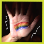 Hand making stop sign with rainbow flag painted on it for LGBTQ ally article