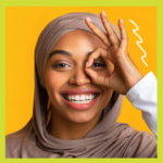 Young woman in head scarf looking through her fingers placed in circle around her eye.