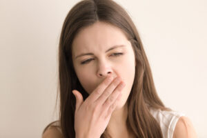 Headshot portrait of yawning young woman. Teenager girl covering her mouth with hand while feeling lack of sleep, fatigue or boredom. Pretty female wants to sleep, tired or lazy. Close up. Front view