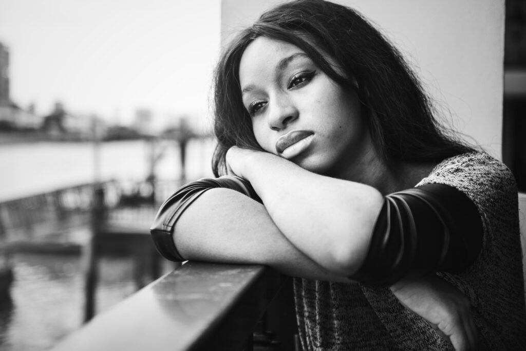 Girl leaning on ledge with head resting on arms with a look of sadness on her face for Sad article.