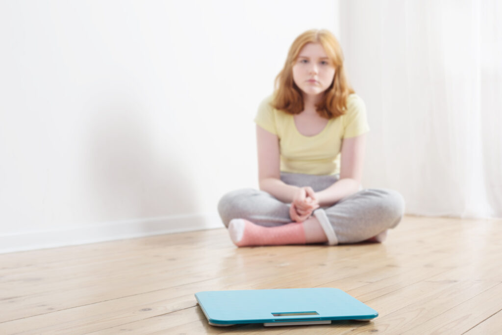 sad teenager girl with scale on wooden floor for suicidal article