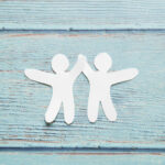 paper cut outs of two people on a blue wooden background for How To Cope With Distressing Things in the News blog