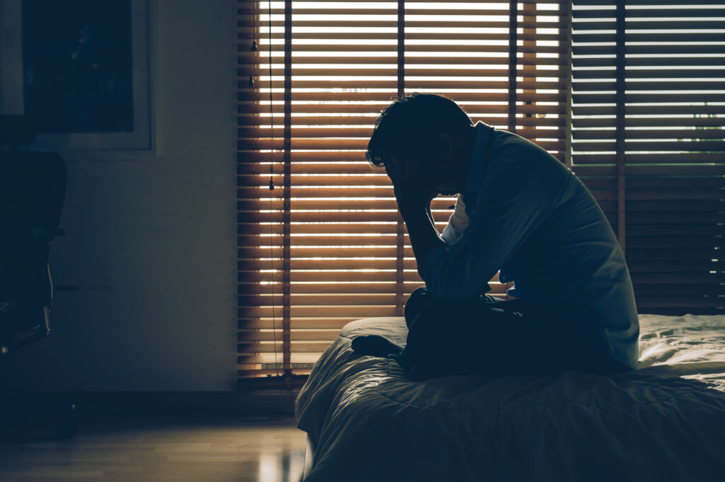 Sadman sitting head in hands on the bed in the dark bedroom with low light environment for What's Happening Between Russia and Ukraine? blog