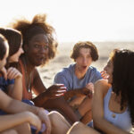 Group of friends having fun talking on the beach for Things to Do After Exams blog