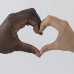 Two hands joining into heart shape, one with black skin and one with white skin.