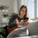 Glum young girl sat down staring at phone for University guide blog