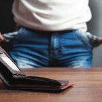 shot of bottom of torso of a person wearing jeans with empty pockets pulled out and an empty wallet on the table - for creating a budget blog 