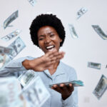 Black woman flicking money notes from hand with palm of other hand with big smile on face for creating a budget blog