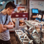 Young asian man is choosing seafood at local chenise market. He is compares prices and seafood.