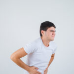 young male in t-shirt suffering from stomachache and looking painful , front view.