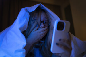 Girl under cover in bed on mobile with shocked face - sexting blog