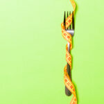 Fork wrapped in measuring tape on green background. Eating disorder concept