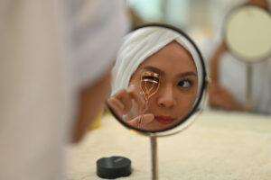 Woman using eyelash curler in front of mirror