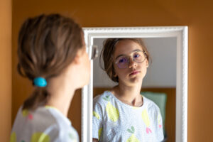 Teenage girl with glasses looking into the mirror at reflection