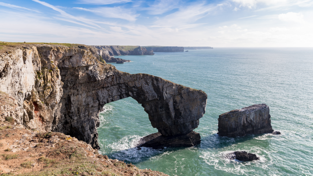 Craig ger y môr gyda chraig yn creu arch i mewn i'r môr glas - Parc Cenedlaethol Penfro