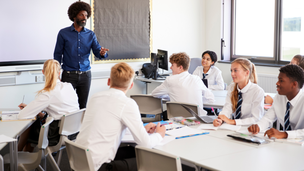 Teacher stood in front of class of seated students, wearing shirts and ties