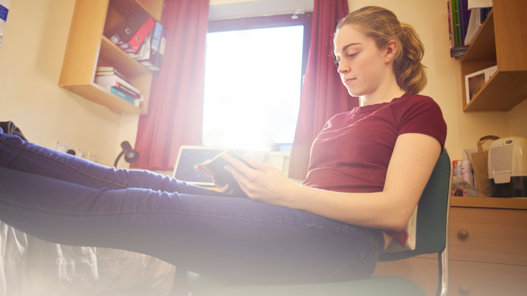 Teen girl sat in form room chair, with feet up on her bed
