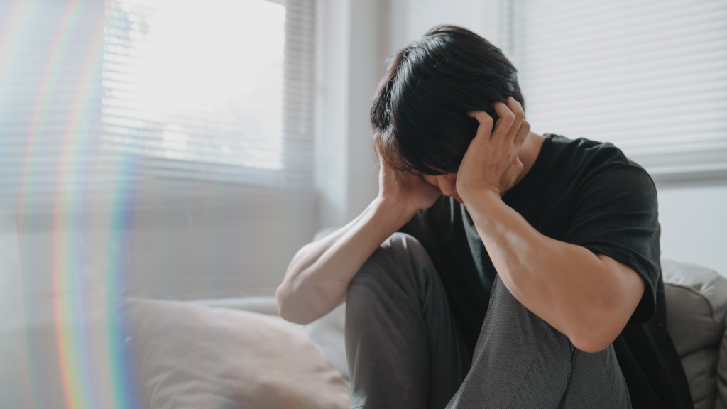 Man sat alone with head in his hands at the bottom of the bed.