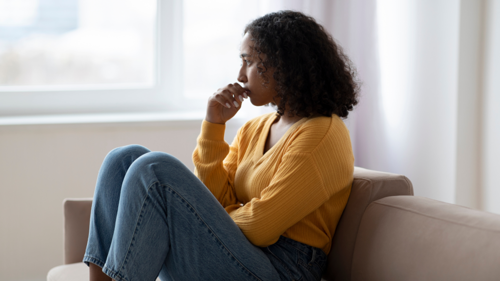 Teenage girl sat on a sofa alone, biting her fingernails. 