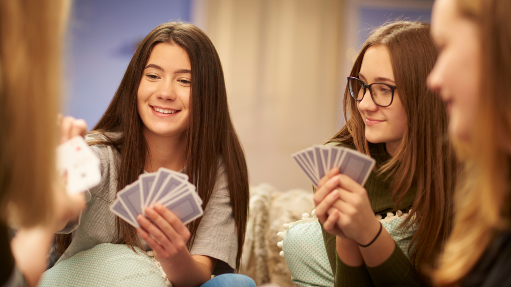 Teenage girls smiling as they're sat in a circle playing card games