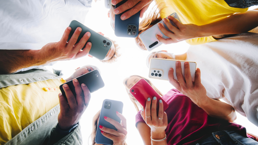 7 young people stood in a circle with their mobile phone out 