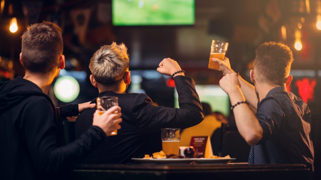 Grŵp o ffrindiau yn yfed mewn bar ac yn gwylio gem ar y teledu