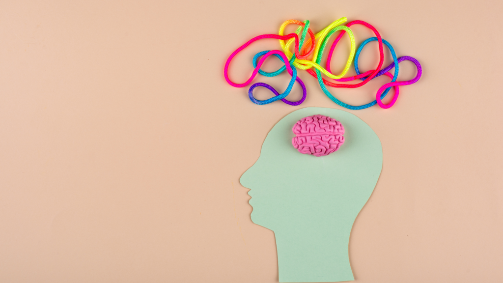 Paper cut out of brain on table, with multi-coloured string above the head