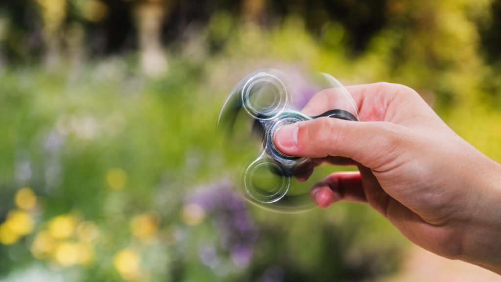Person yn defnyddio 'fidget spinner' mewn gardd. Teclynnau synhwyrol awtistiaeth 