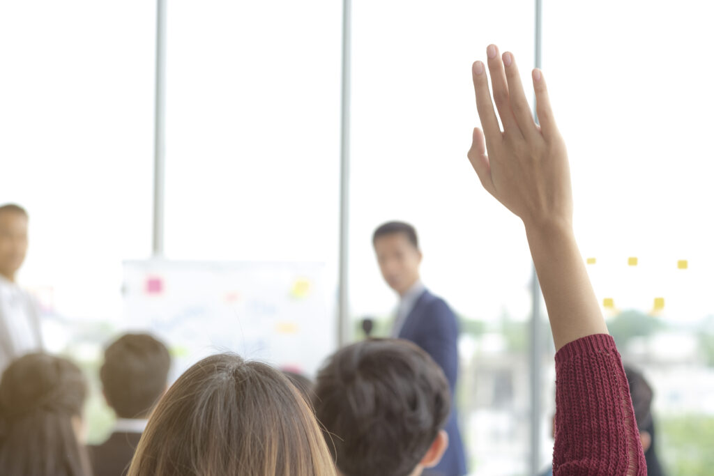 A woman holding her hand up to ask a question in a public meeting 