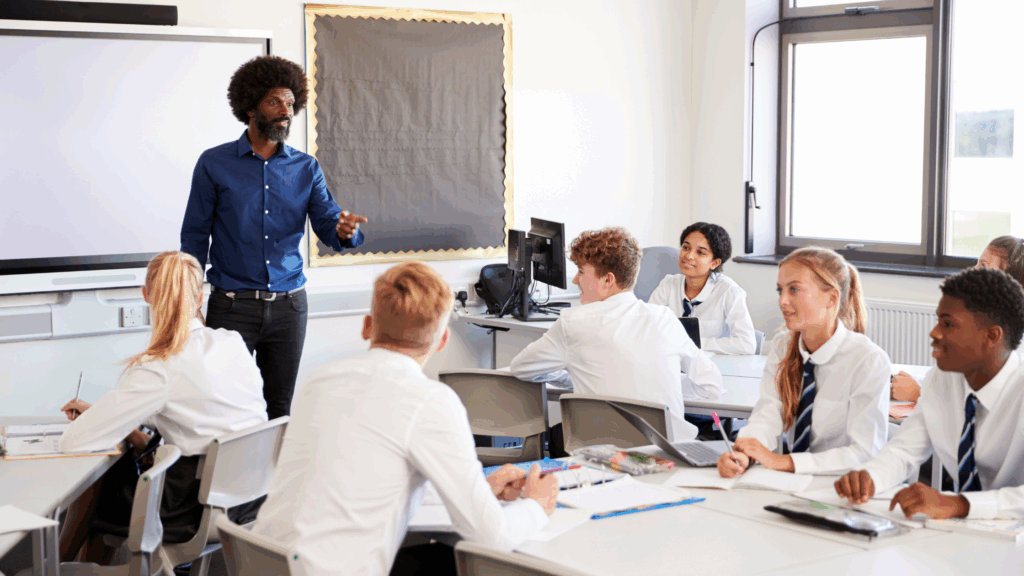 Teacher talking at the front of secondary school classroom full with students