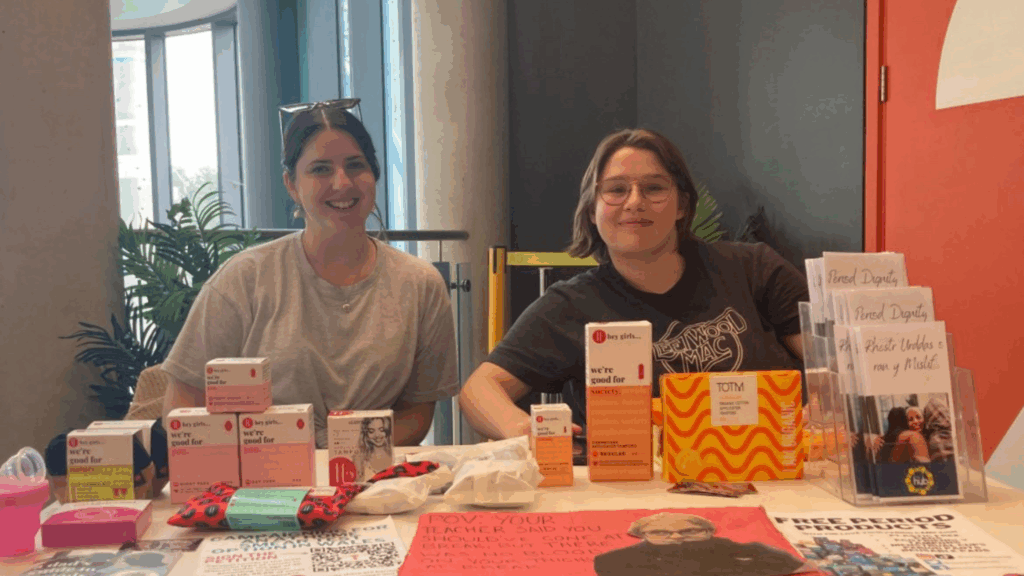 Two Love Your Period Campaigners sat at a stall with lots of period products 