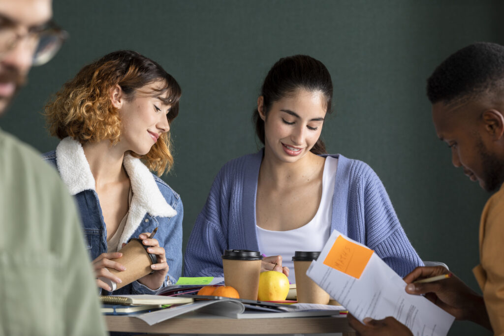 Four young people around a table, two women are looking at their notes and smiling 