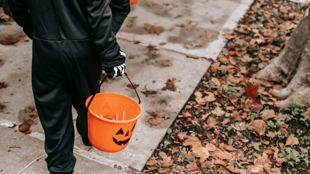 Young child trick or treating dressed as a skeleton, holding a pumpkin bucket for sweets